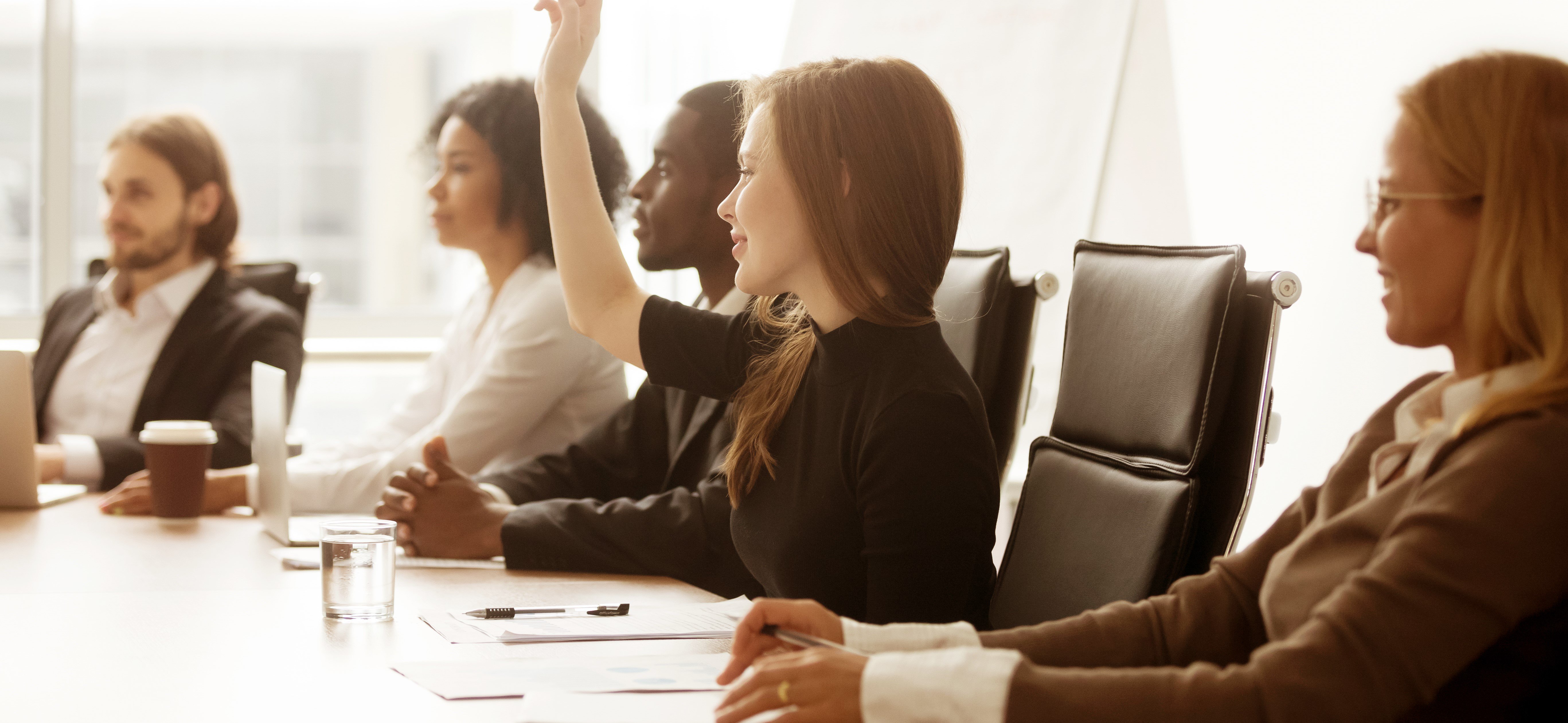 board members sitting at a table, one raising her hand.