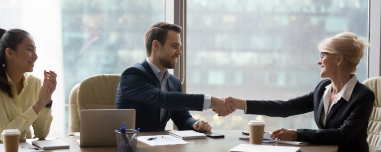 Two women and a man shaking hands at a conference table